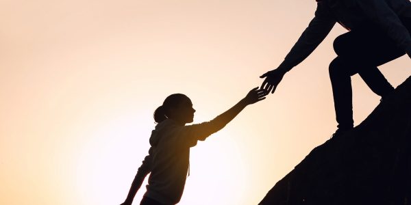 Silhouettes of man and woman helping each other to climb on hill against sunset